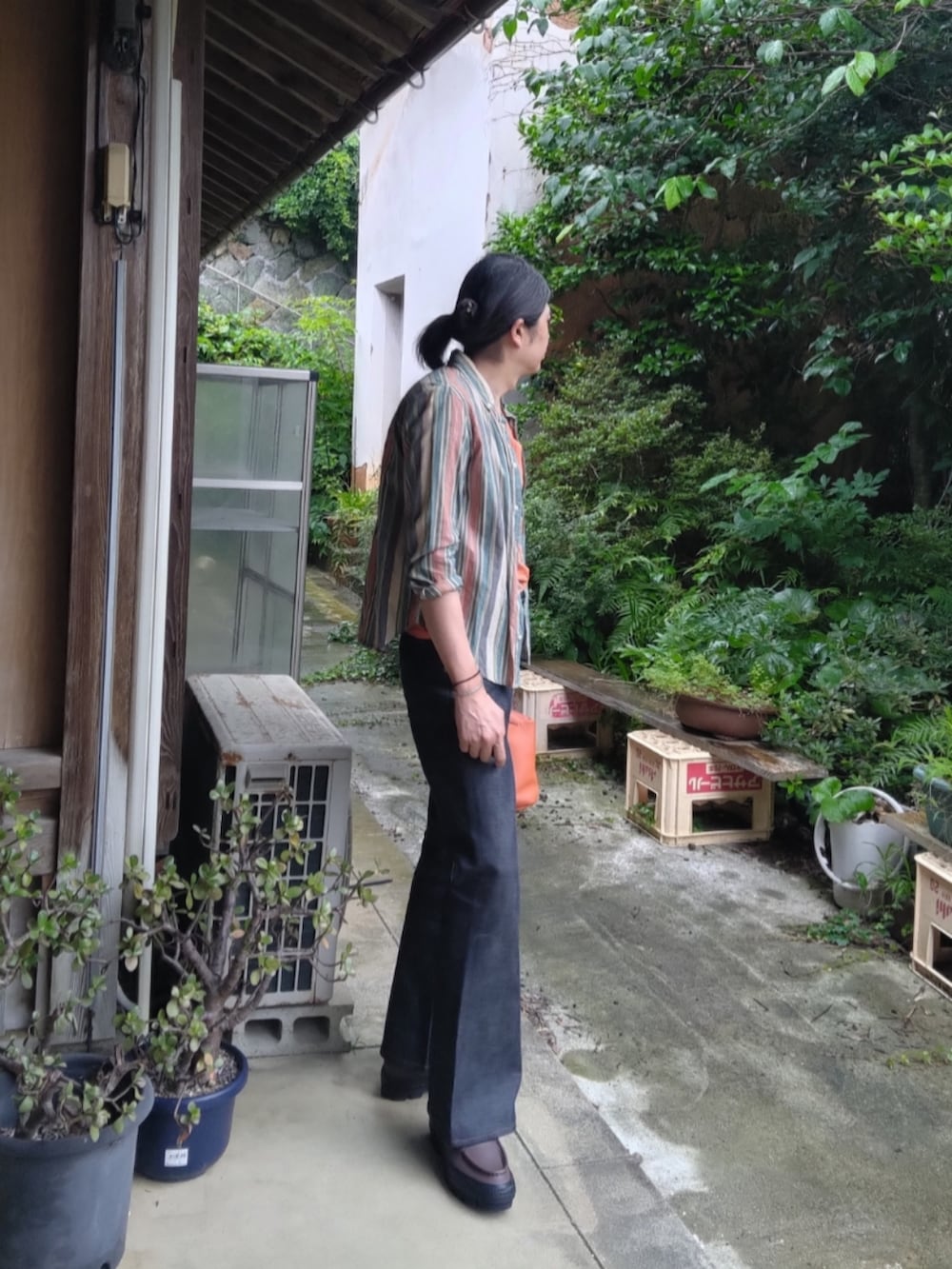 オレンジ系のTシャツ/カットソー、ブルー系のデニムパンツ、ブラウン系のスニーカーを着用したメンズの夏コーディネートの2枚目の写真