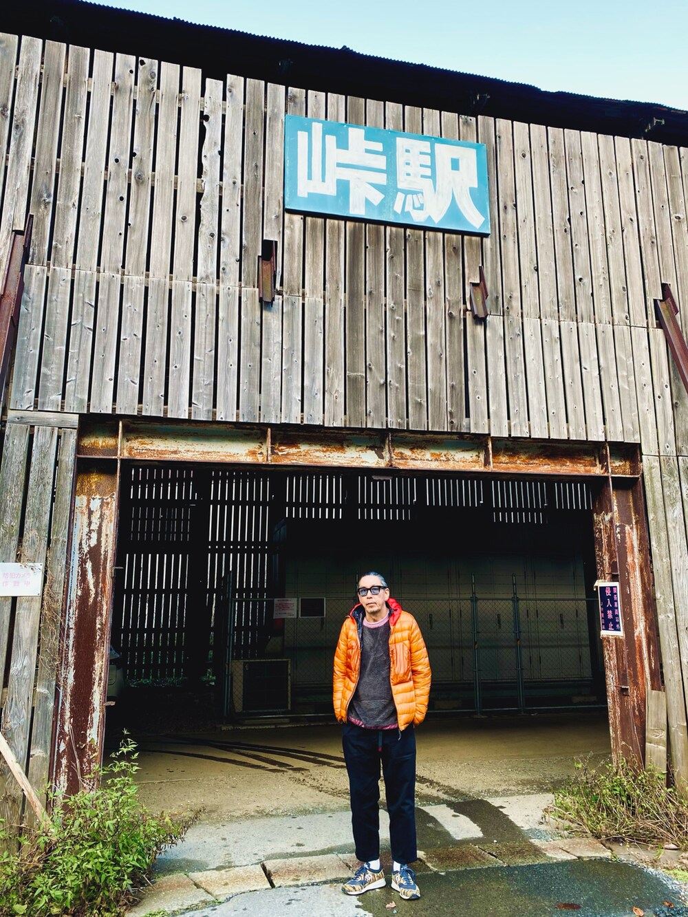 オレンジ系のダウンジャケット/コート、グレー系のその他トップス、ブラック系のパンツを着用したメンズの秋コーディネートの2枚目の写真