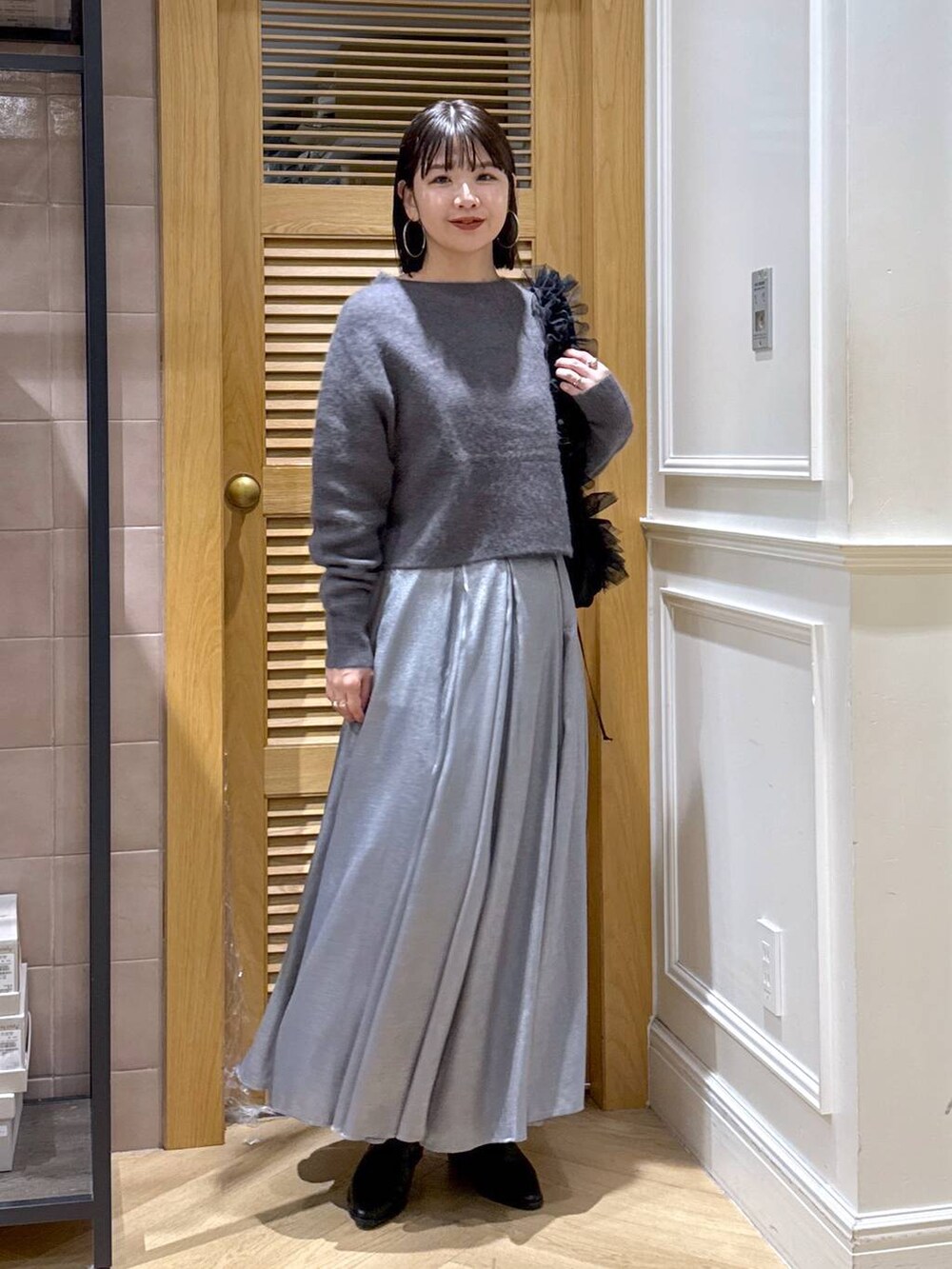 グレー系のニット/セーター、グレー系のスカート、ブラック系のショルダーバッグを着用したレディースの秋コーディネートの3枚目の写真