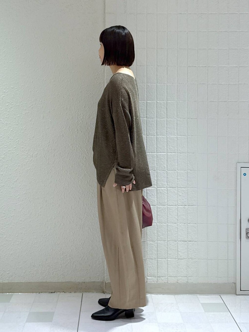 ベージュ系のスラックス、ブラック系のブーツ、レッド系のショルダーバッグを着用したレディースの秋コーディネートの5枚目の写真