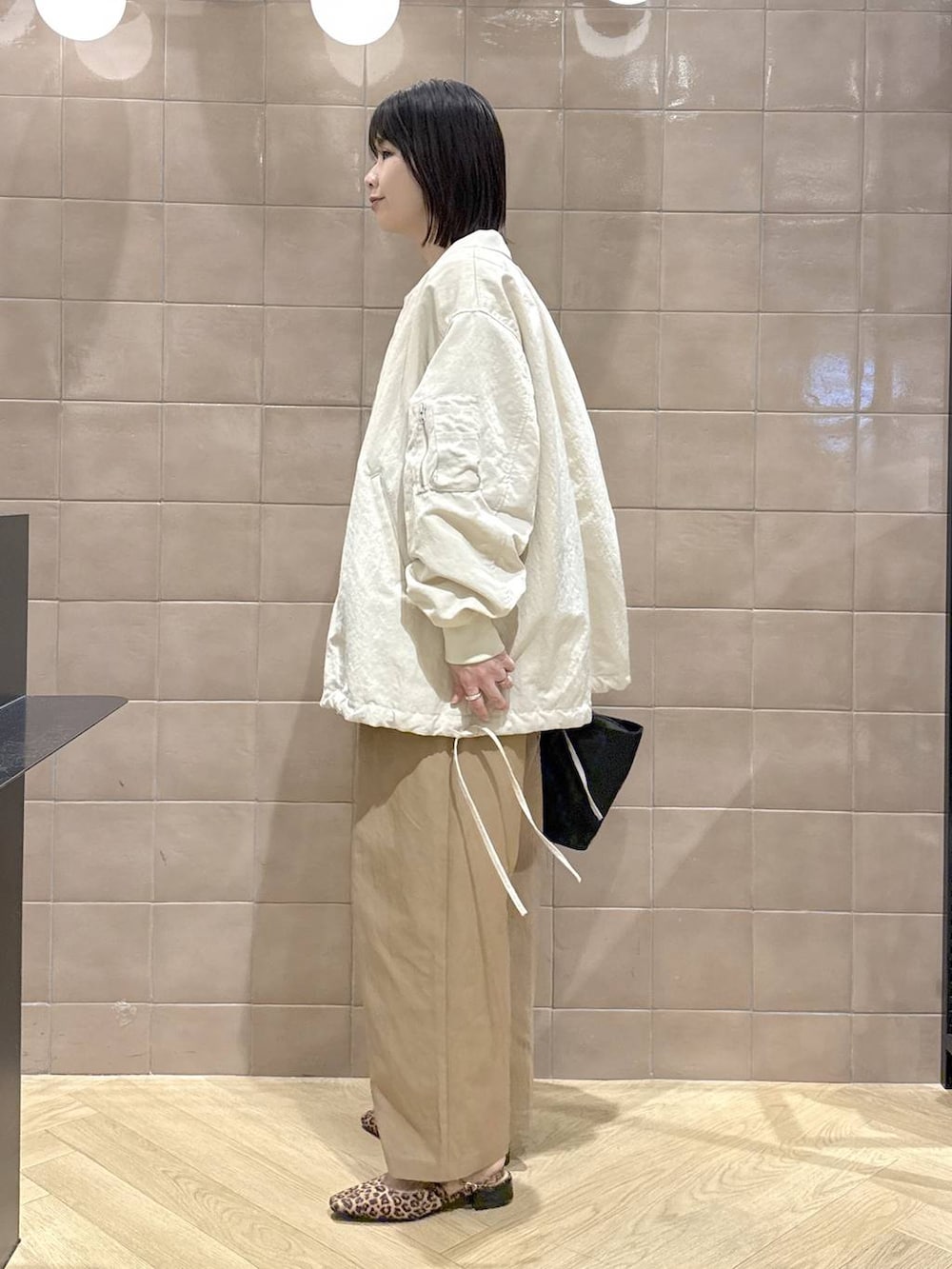 ベージュ系のMA-1、ブラック系のトートバッグ、ブラウン系のチノパンツを着用したレディースの春コーディネートの5枚目の写真