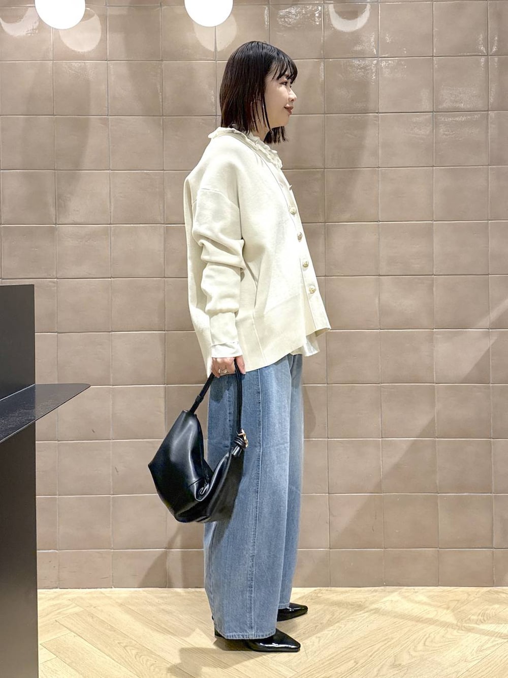 ブルー系のデニムパンツ、ホワイト系のカーディガン/ボレロ、ブラック系のショルダーバッグを着用したレディースの冬コーディネートの2枚目の写真