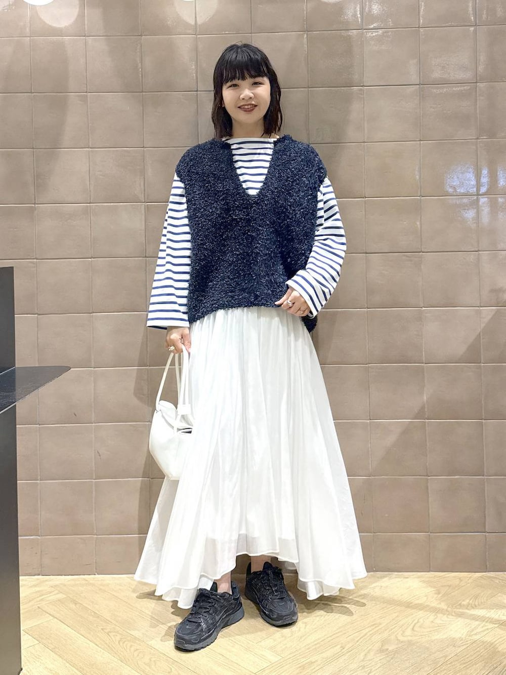 ホワイト系のスカート、ブルー系のベスト、ホワイト系のショルダーバッグを着用したレディースの冬コーディネートの2枚目の写真