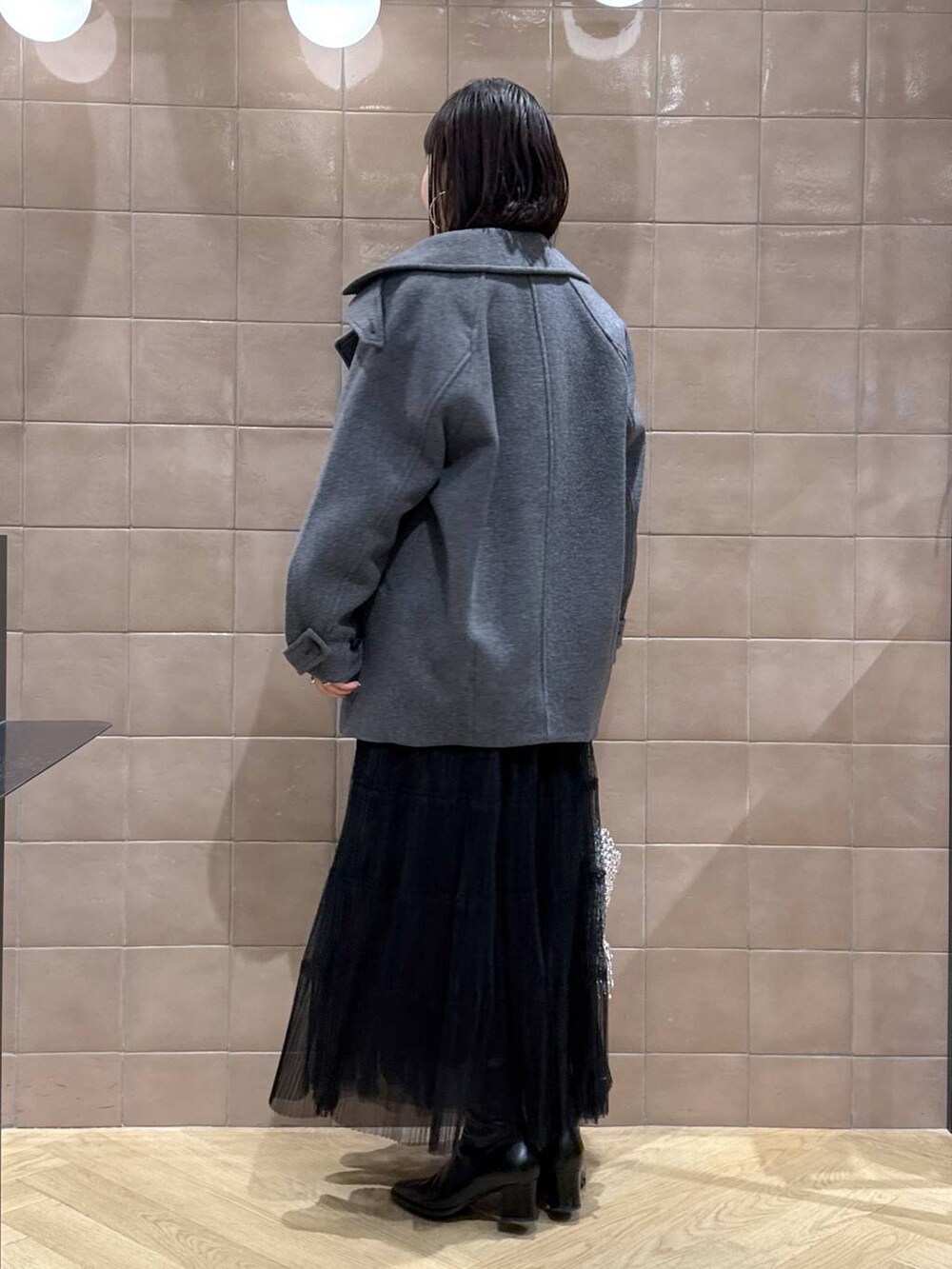 グレー系のピーコート、ブラック系のスカート、グレー系のカーディガン/ボレロを着用したレディースの春コーディネートの3枚目の写真
