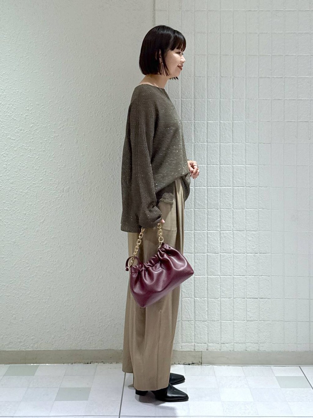 ベージュ系のスラックス、ブラック系のブーツ、レッド系のショルダーバッグを着用したレディースの秋コーディネートの3枚目の写真