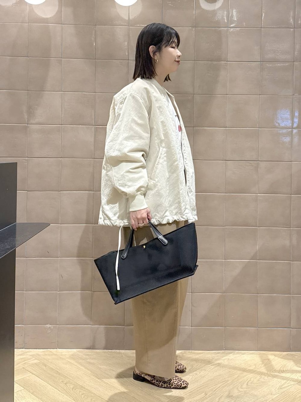 ベージュ系のMA-1、ブラック系のトートバッグ、ブラウン系のチノパンツを着用したレディースの春コーディネートの3枚目の写真