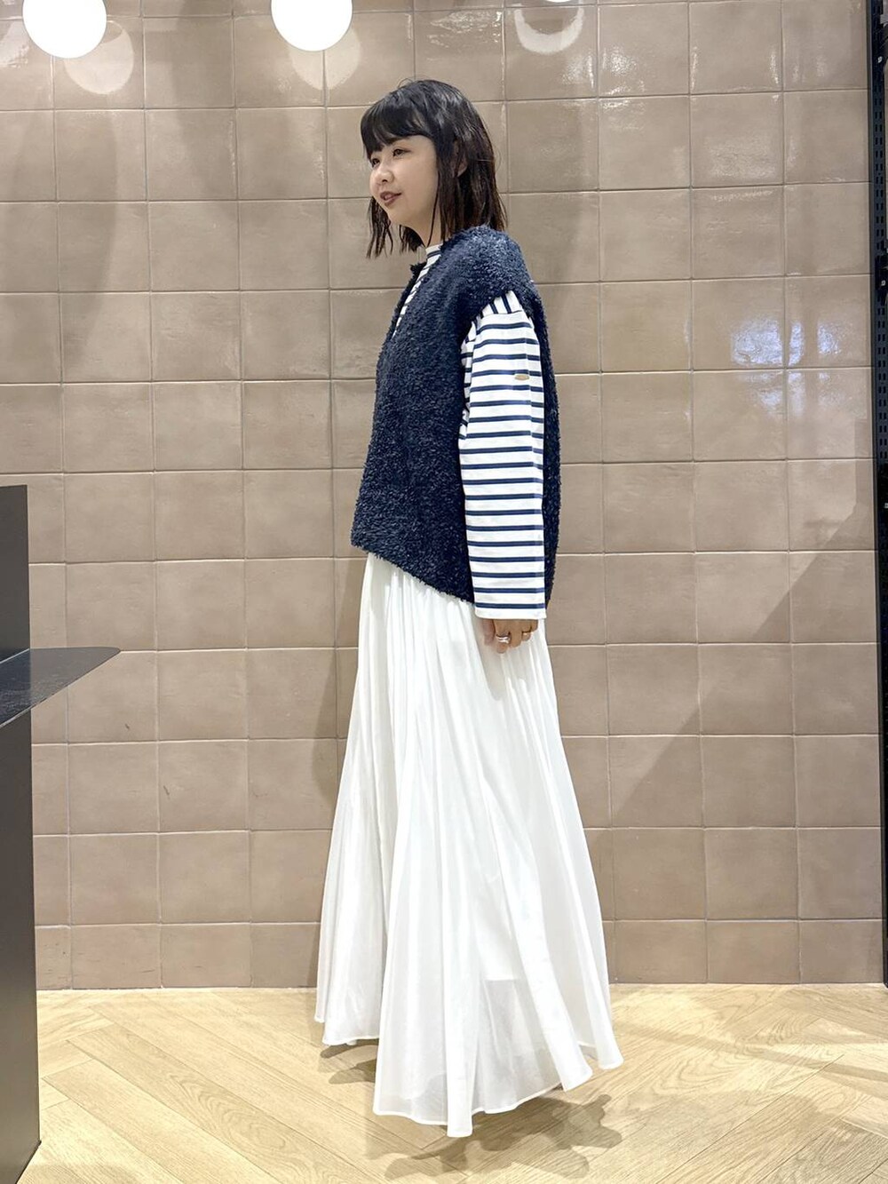 ホワイト系のスカート、ブルー系のベスト、ホワイト系のショルダーバッグを着用したレディースの冬コーディネートの5枚目の写真