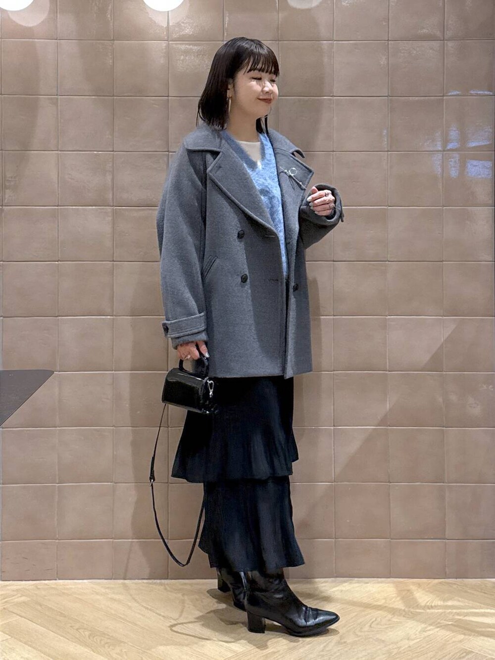 グレー系のピーコート、ホワイト系のTシャツ/カットソー、ブラック系のスカートを着用したレディースの冬コーディネートの2枚目の写真