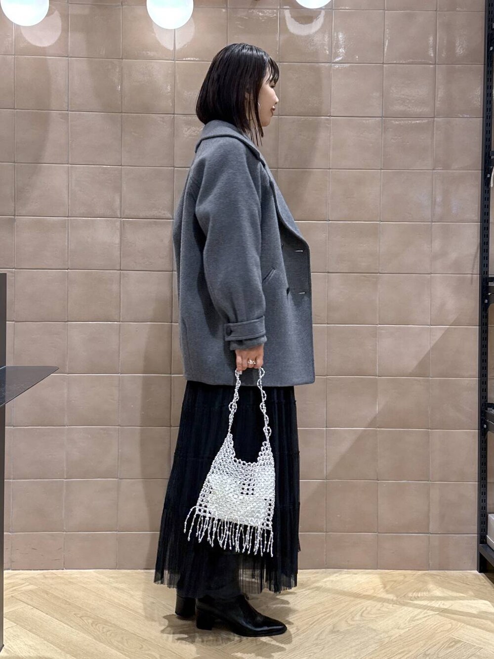 グレー系のピーコート、ブラック系のスカート、グレー系のカーディガン/ボレロを着用したレディースの春コーディネートの2枚目の写真