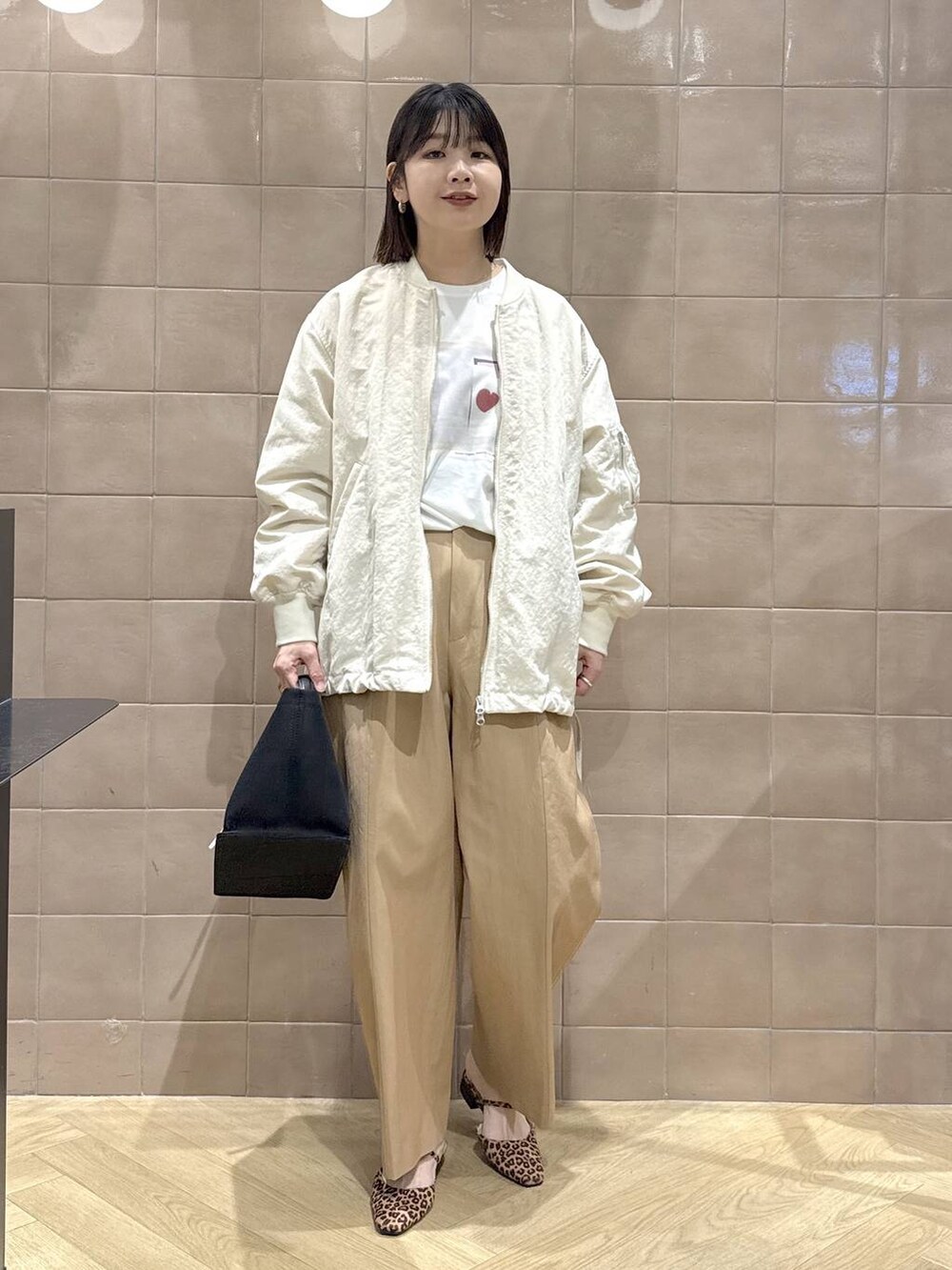 ベージュ系のMA-1、ブラック系のトートバッグ、ブラウン系のチノパンツを着用したレディースの春コーディネートの2枚目の写真