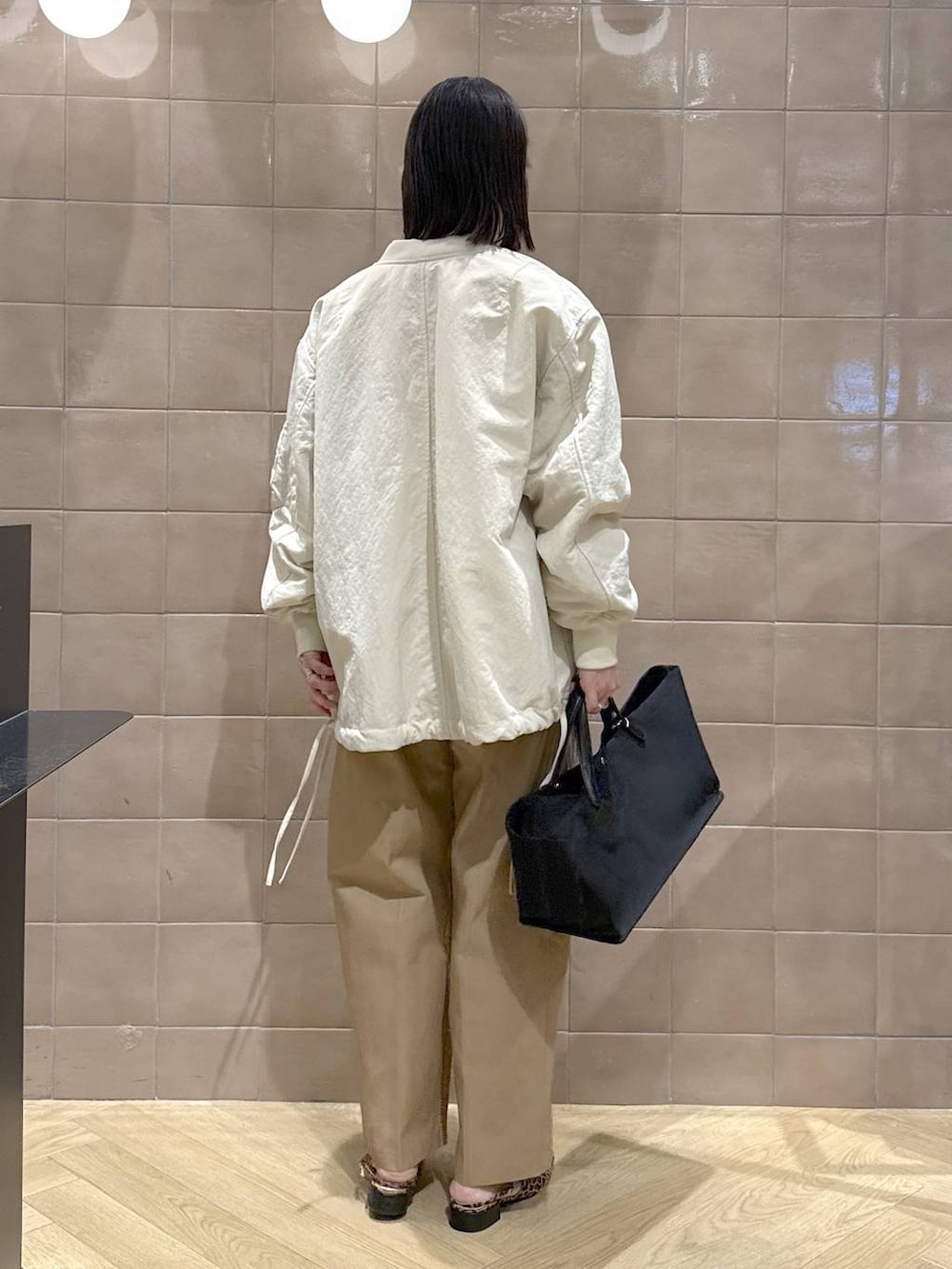 ベージュ系のMA-1、ブラック系のトートバッグ、ブラウン系のチノパンツを着用したレディースの春コーディネートの4枚目の写真