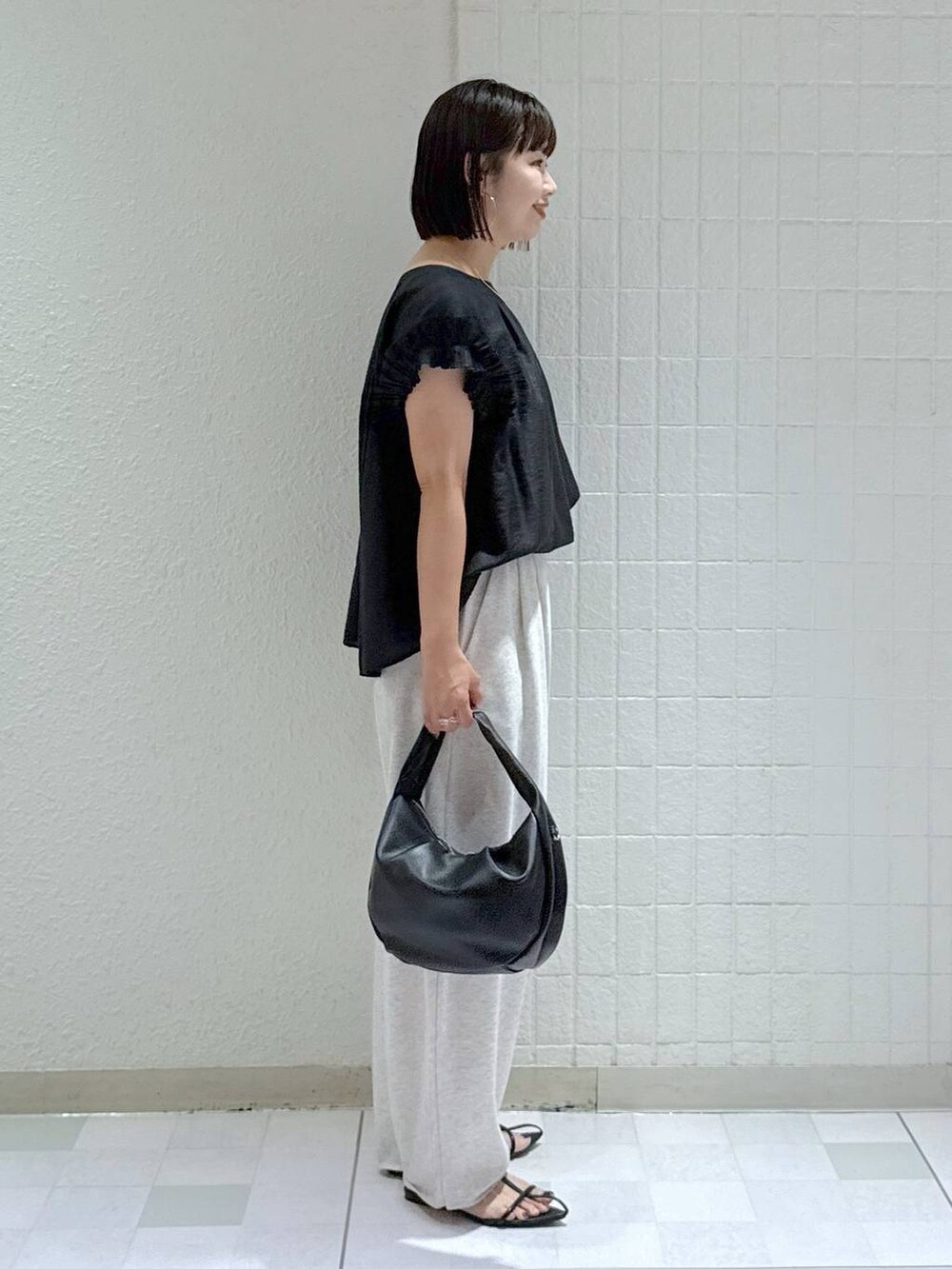 ブラック系のハンドバッグ、ブラック系のサンダル、グレー系のスウェットパンツを着用したレディースの夏コーディネートの3枚目の写真