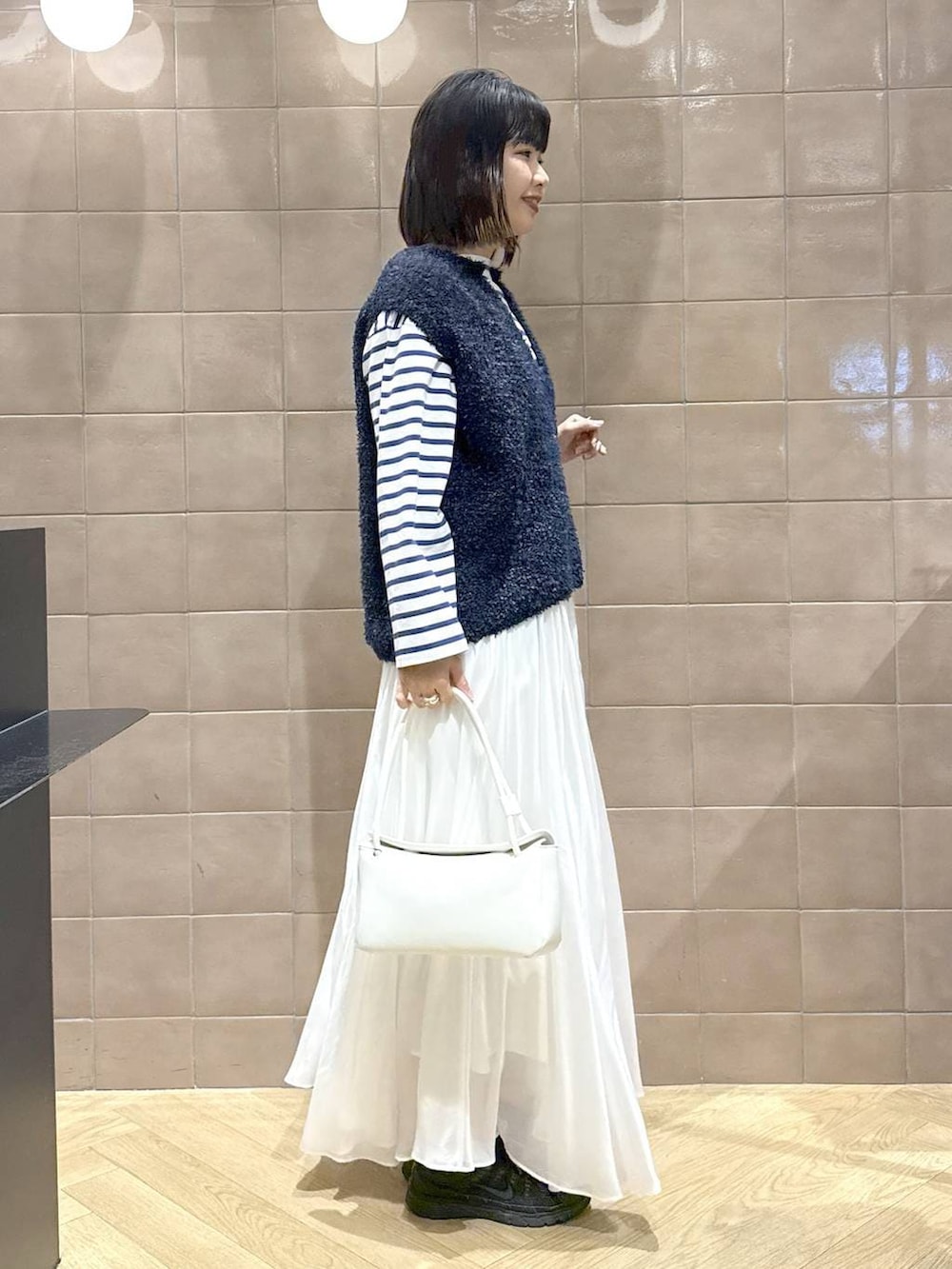 ホワイト系のスカート、ブルー系のベスト、ホワイト系のショルダーバッグを着用したレディースの冬コーディネートの3枚目の写真