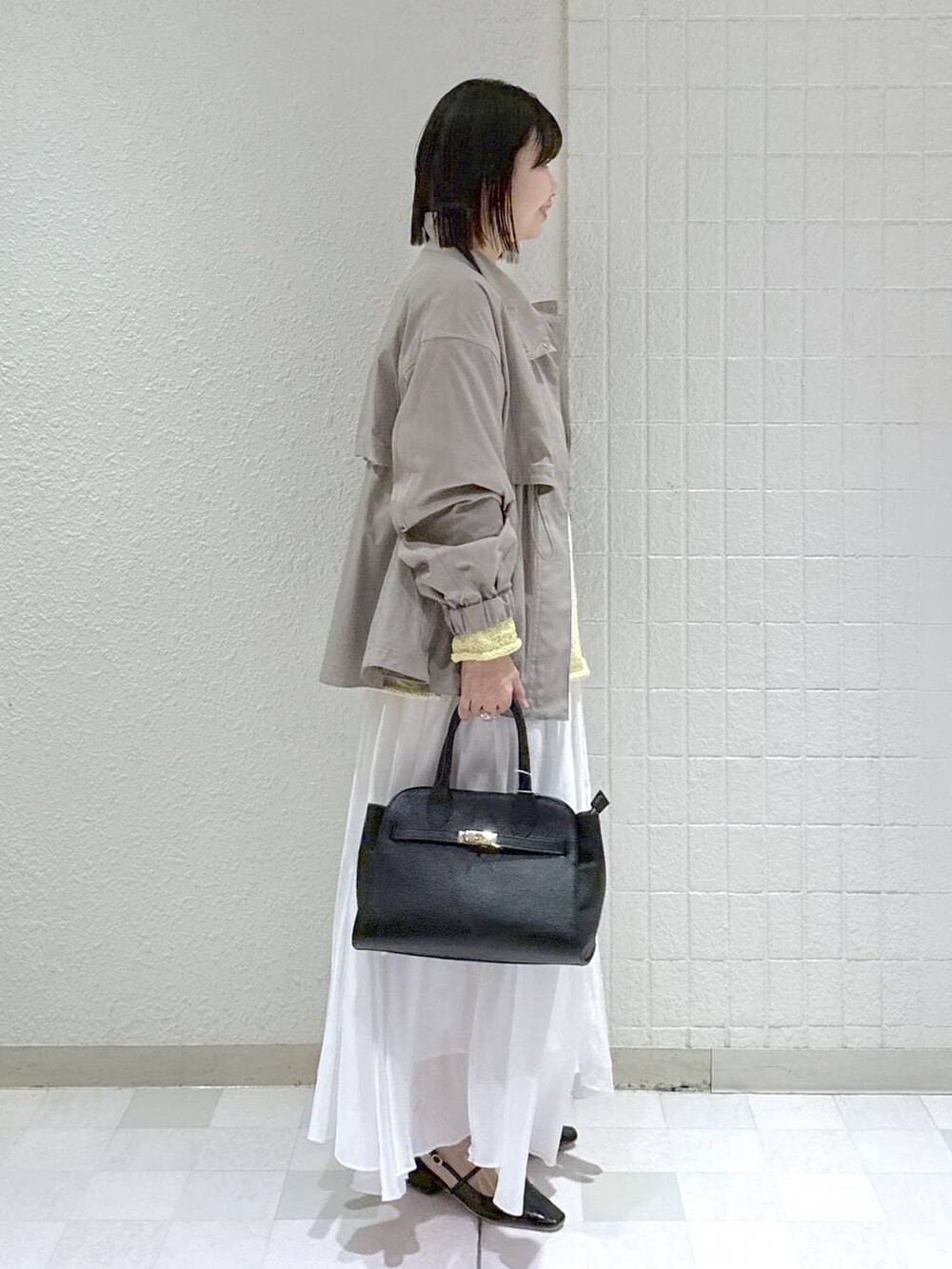 グレー系のブルゾン、ホワイト系のスカート、ブラック系のショルダーバッグを着用したレディースの春コーディネートの2枚目の写真