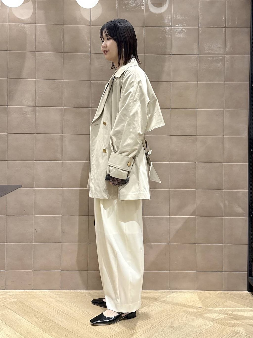ホワイト系のスラックス、ブラック系のショルダーバッグ、ベージュ系のトレンチコートを着用したレディースの春コーディネートの4枚目の写真