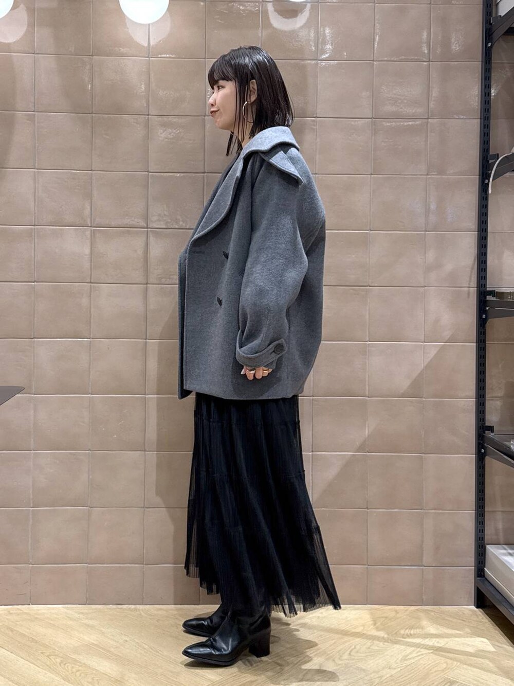 グレー系のピーコート、ブラック系のスカート、グレー系のカーディガン/ボレロを着用したレディースの春コーディネートの4枚目の写真