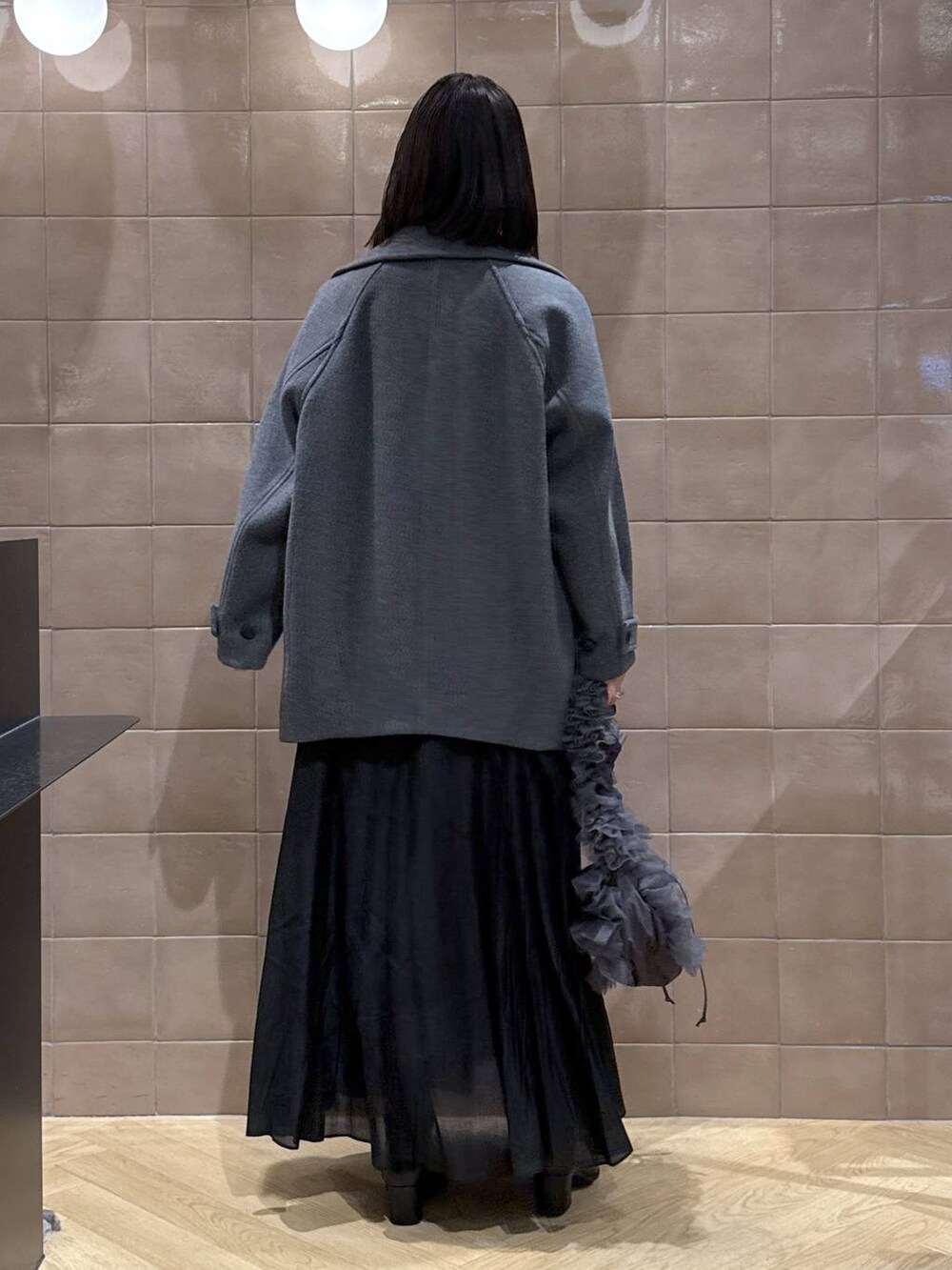 グレー系のピーコート、グレー系のニット/セーター、ブラック系のスカートを着用したレディースの冬コーディネートの3枚目の写真