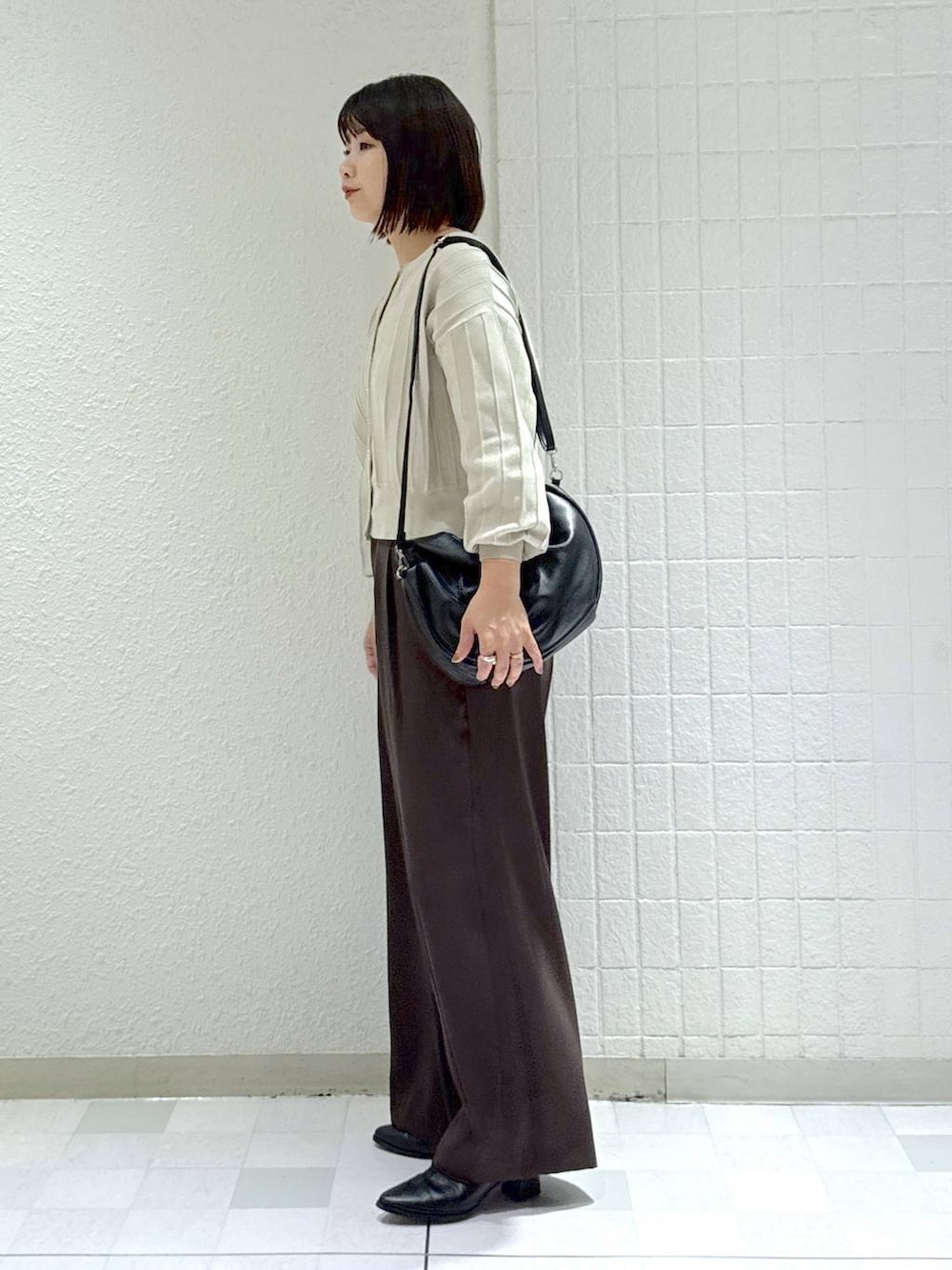 ブラック系のハンドバッグ、ベージュ系のカーディガン/ボレロ、ブラック系のブーツを着用したレディースの秋コーディネートの5枚目の写真