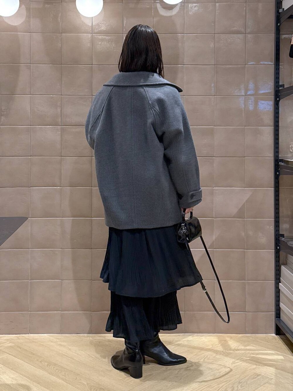 グレー系のピーコート、ホワイト系のTシャツ/カットソー、ブラック系のスカートを着用したレディースの冬コーディネートの3枚目の写真