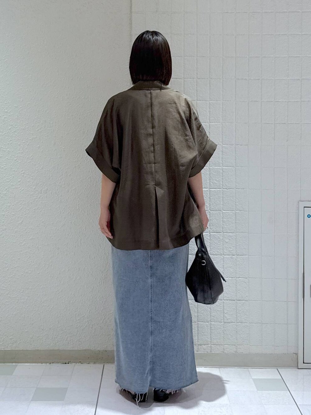 ブラック系のハンドバッグ、ブラック系のサンダル、ブルー系のデニムスカートを着用したレディースの秋コーディネートの3枚目の写真