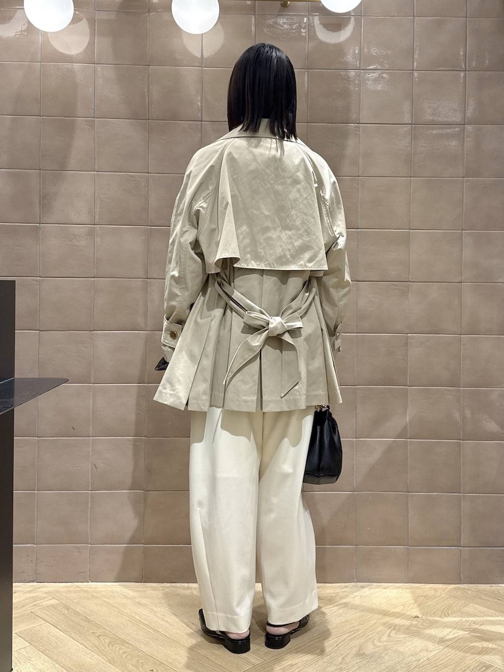 ホワイト系のスラックス、ブラック系のショルダーバッグ、ベージュ系のトレンチコートを着用したレディースの春コーディネートの3枚目の写真