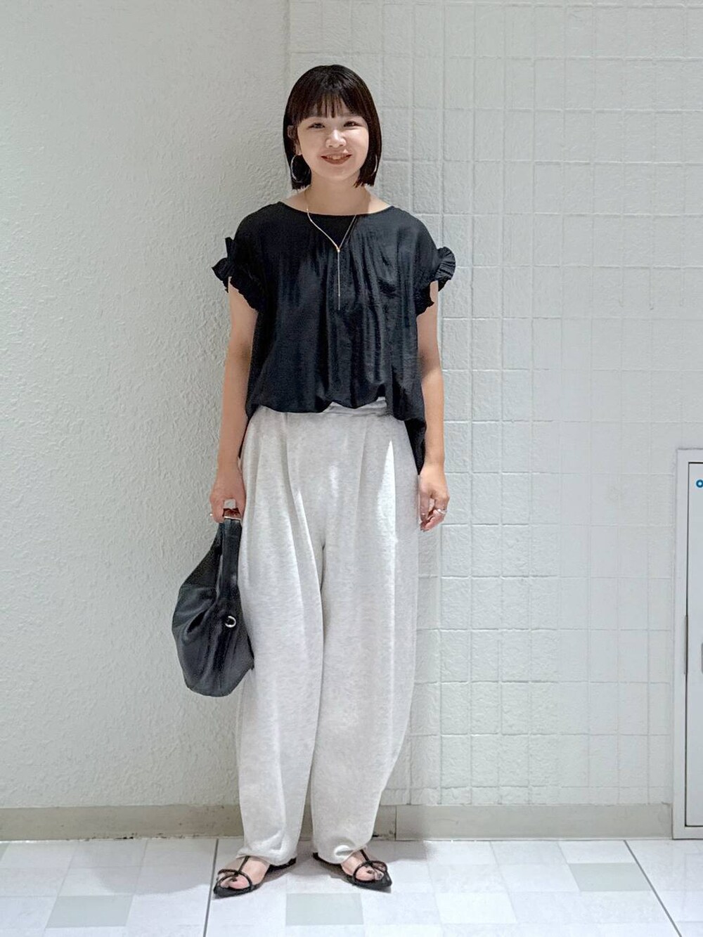 ブラック系のハンドバッグ、ブラック系のサンダル、グレー系のスウェットパンツを着用したレディースの夏コーディネートの2枚目の写真