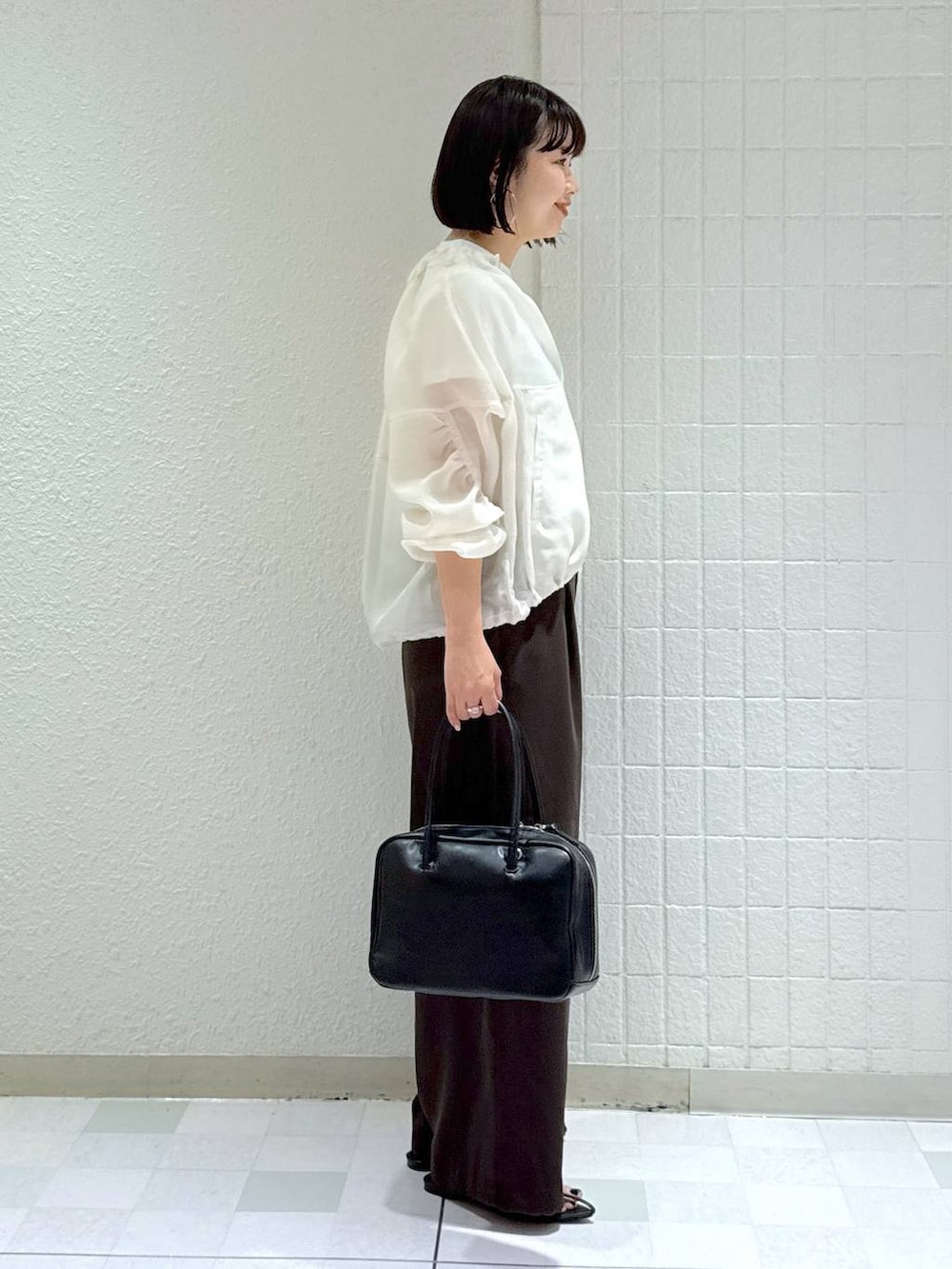 ブラック系のボストンバッグ、ホワイト系のブルゾン、ブラック系のサンダルを着用したレディースの春コーディネートの3枚目の写真