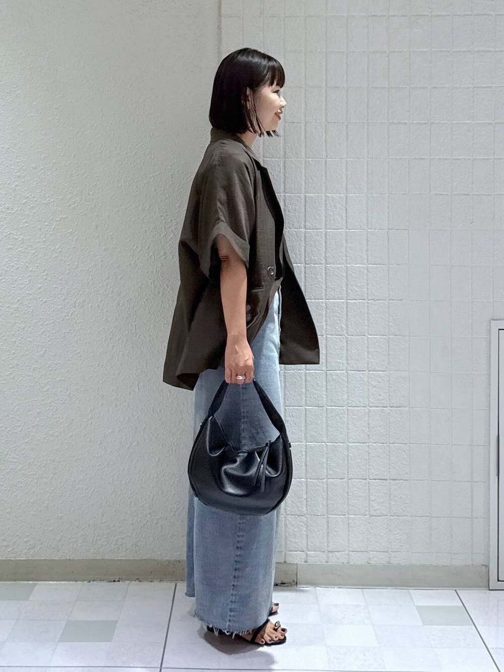 ブラック系のハンドバッグ、ブラック系のサンダル、ブルー系のデニムスカートを着用したレディースの秋コーディネートの2枚目の写真