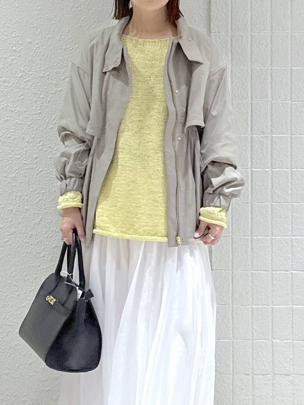 グレー系のブルゾン、ホワイト系のスカート、ブラック系のショルダーバッグを着用したレディースの春コーディネートの5枚目の写真