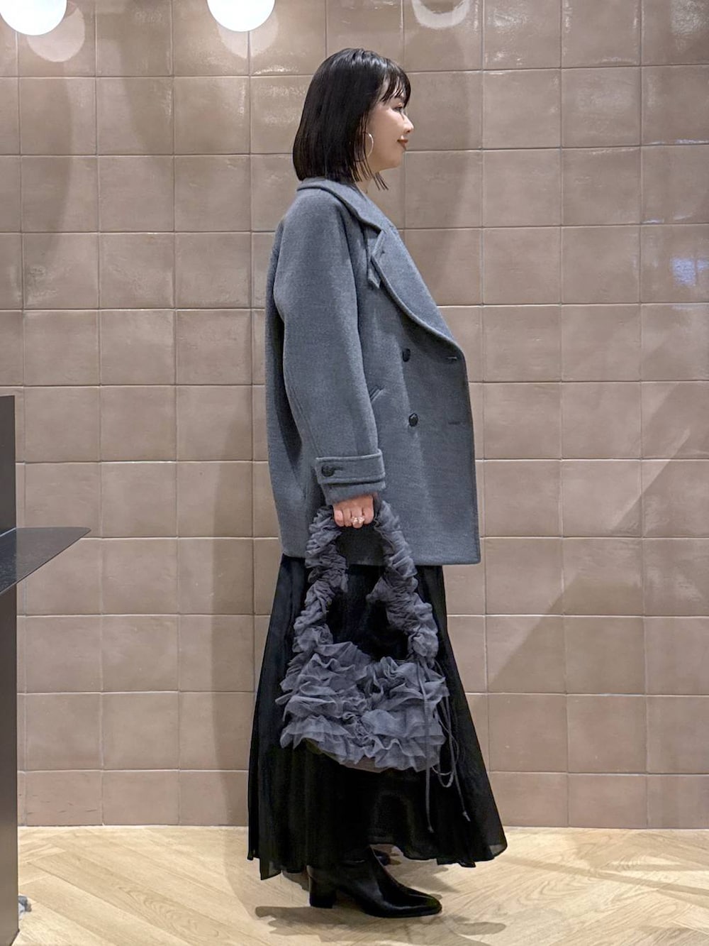 グレー系のピーコート、グレー系のニット/セーター、ブラック系のスカートを着用したレディースの冬コーディネートの2枚目の写真