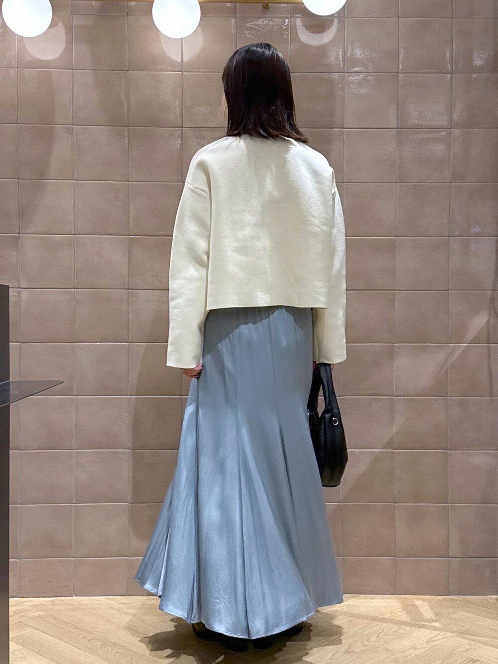 ブラック系のハンドバッグ、ホワイト系のカーディガン/ボレロ、ブルー系のスカートを着用したレディースの秋コーディネートの4枚目の写真