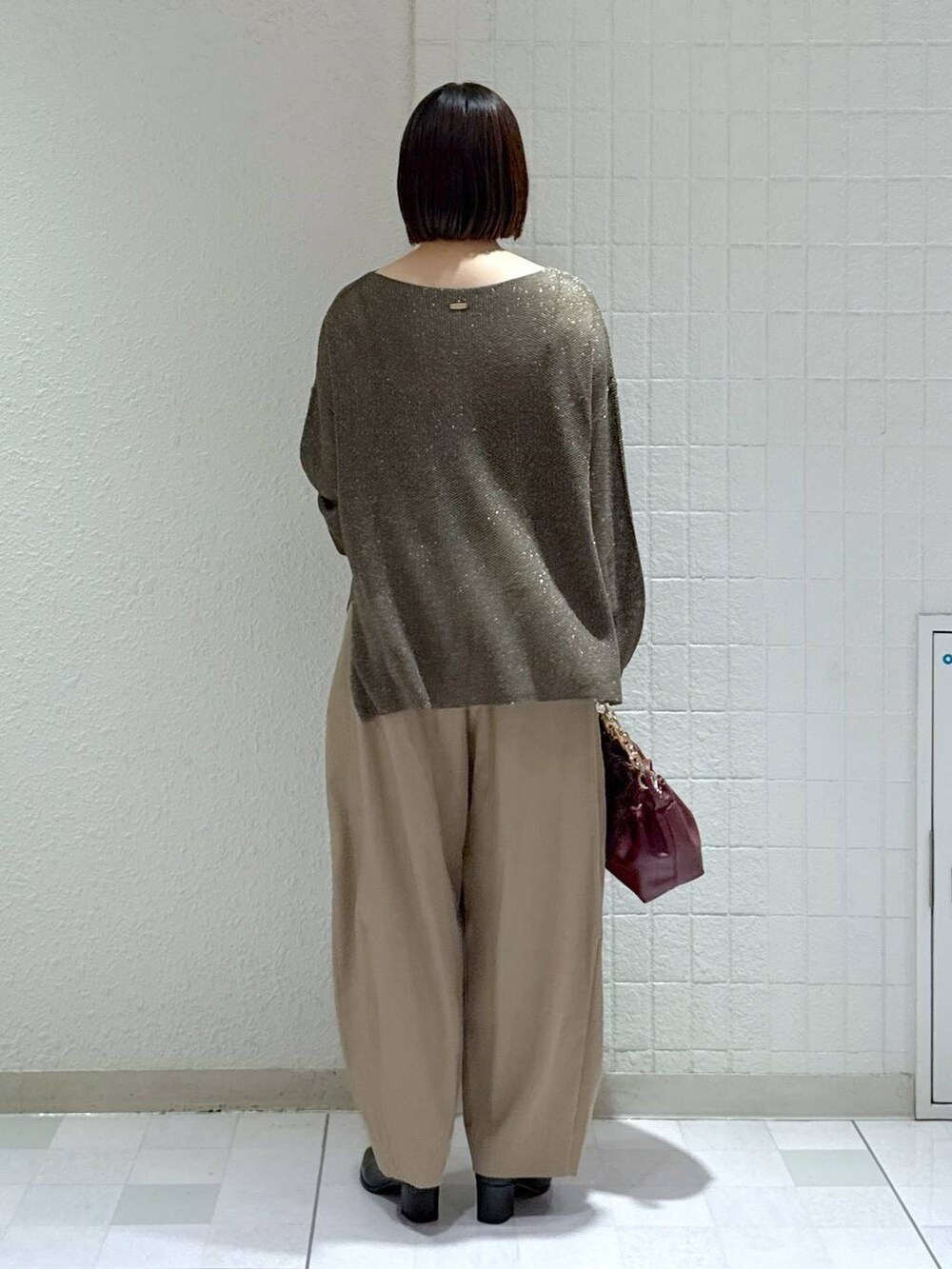 ベージュ系のスラックス、ブラック系のブーツ、レッド系のショルダーバッグを着用したレディースの秋コーディネートの4枚目の写真