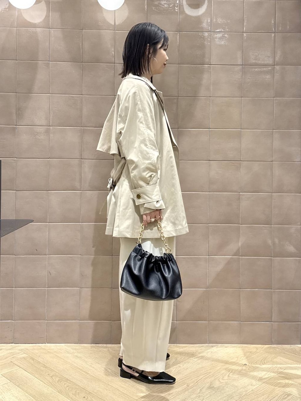 ホワイト系のスラックス、ブラック系のショルダーバッグ、ベージュ系のトレンチコートを着用したレディースの春コーディネートの2枚目の写真