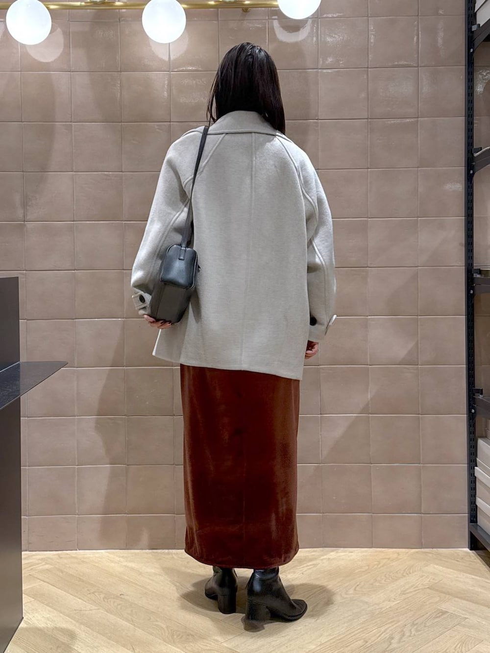 ベージュ系のピーコート、ブラック系のブーツ、ブラウン系のワンピースを着用したレディースの冬コーディネートの2枚目の写真