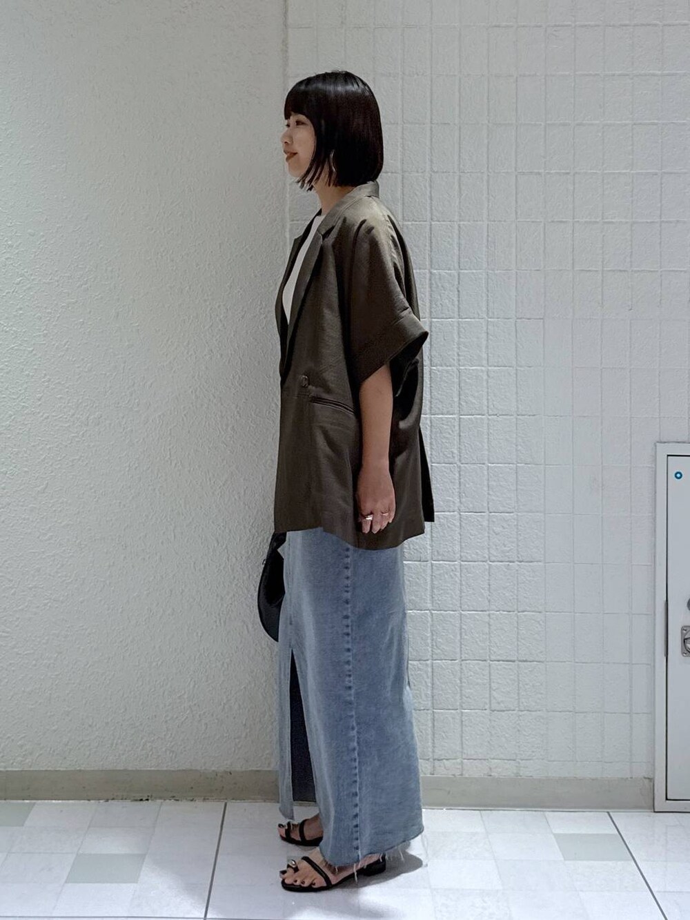 ブラック系のハンドバッグ、ブラック系のサンダル、ブルー系のデニムスカートを着用したレディースの秋コーディネートの4枚目の写真