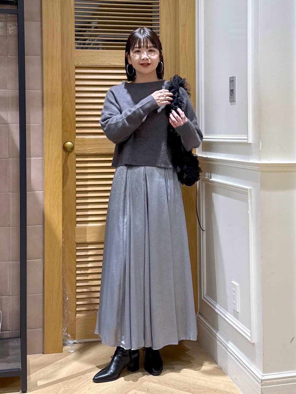 グレー系のニット/セーター、グレー系のスカート、ブラック系のショルダーバッグを着用したレディースの秋コーディネートの2枚目の写真