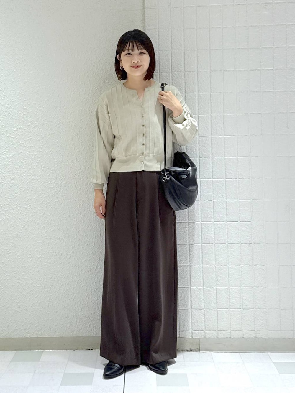 ブラック系のハンドバッグ、ベージュ系のカーディガン/ボレロ、ブラック系のブーツを着用したレディースの秋コーディネートの2枚目の写真