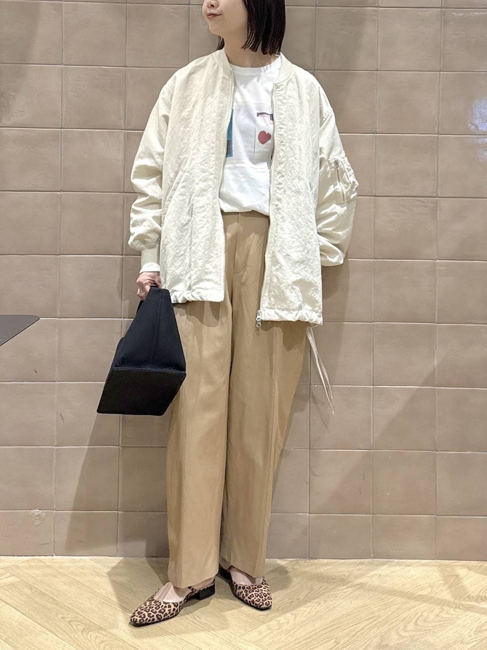 ベージュ系のMA-1、ブラック系のトートバッグ、ブラウン系のチノパンツを着用したレディースの春コーディネートの6枚目の写真