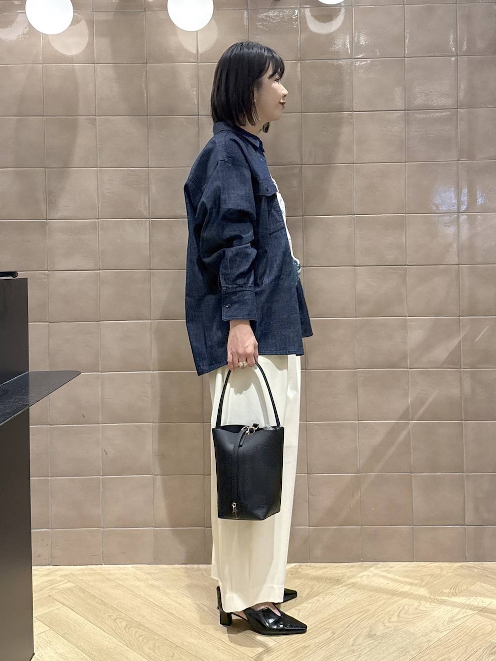 ホワイト系のスラックス、ブラック系のパンプス、ブラック系のショルダーバッグを着用したレディースの春コーディネートの4枚目の写真