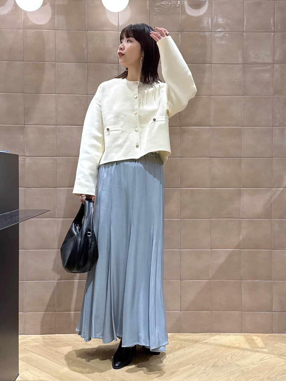 ブラック系のハンドバッグ、ホワイト系のカーディガン/ボレロ、ブルー系のスカートを着用したレディースの秋コーディネートの2枚目の写真