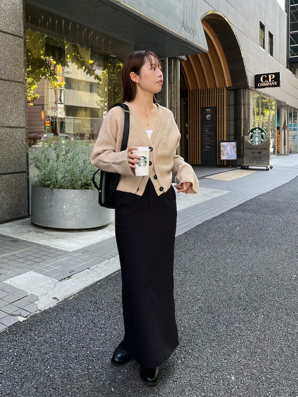 ブラック系のショルダーバッグ、ベージュ系のカーディガン/ボレロ、ブラック系のスカートを着用したレディースの秋コーディネートの2枚目の写真