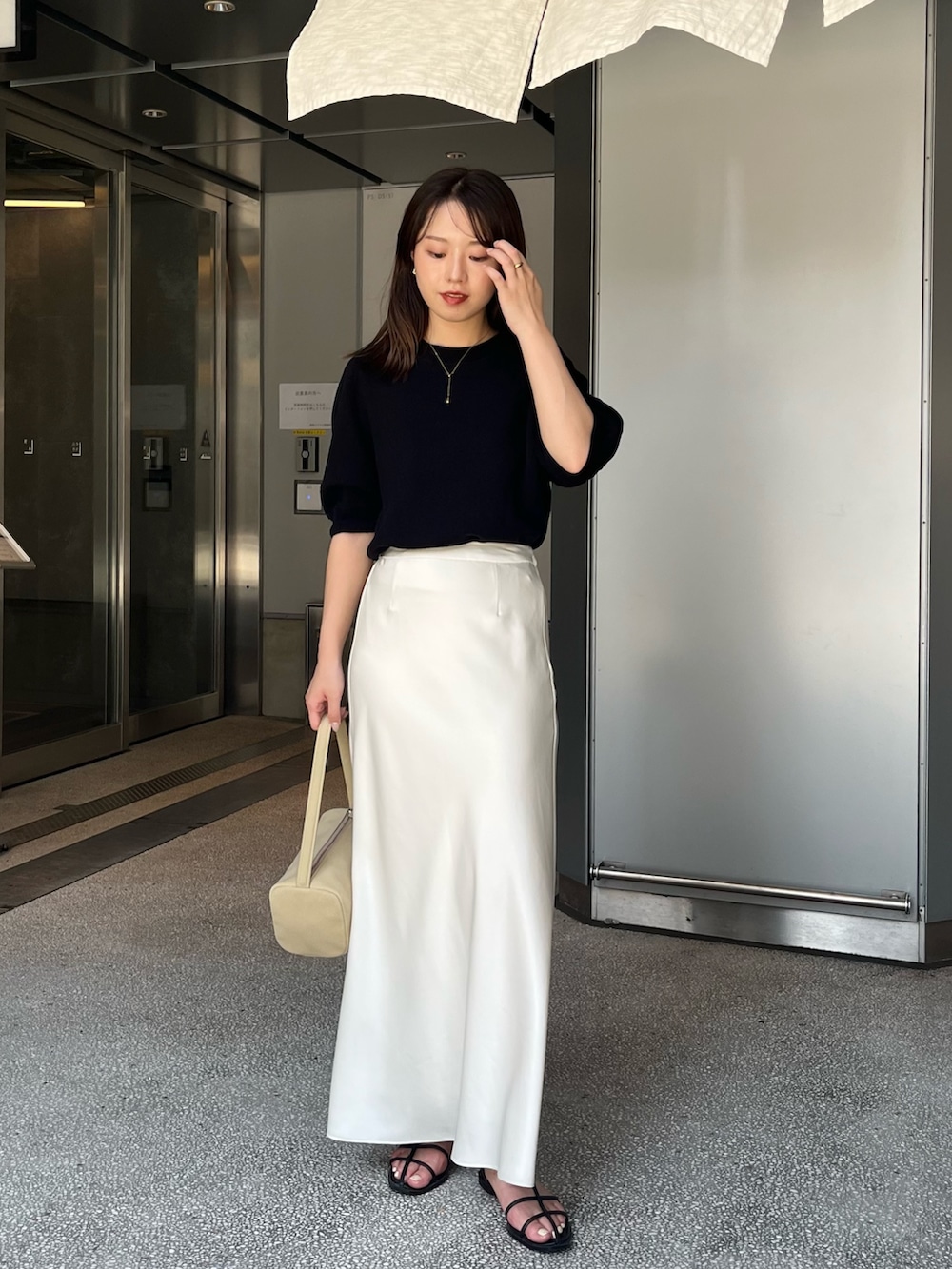ブラック系のニット/セーター、ホワイト系のスカート、ブラック系のサンダルを着用したレディースの夏コーディネートの3枚目の写真