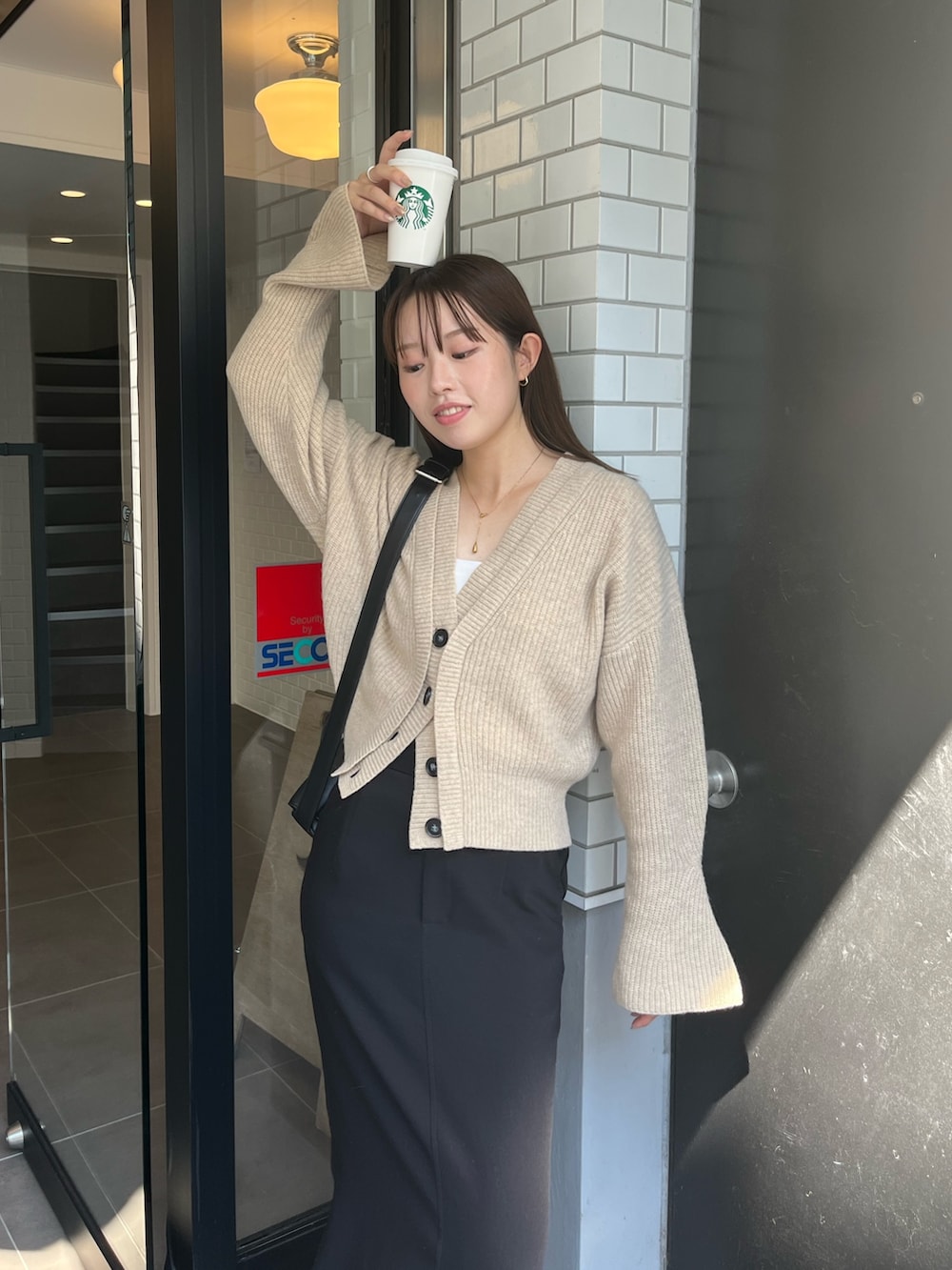 ブラック系のショルダーバッグ、ベージュ系のカーディガン/ボレロ、ブラック系のスカートを着用したレディースの秋コーディネートの4枚目の写真