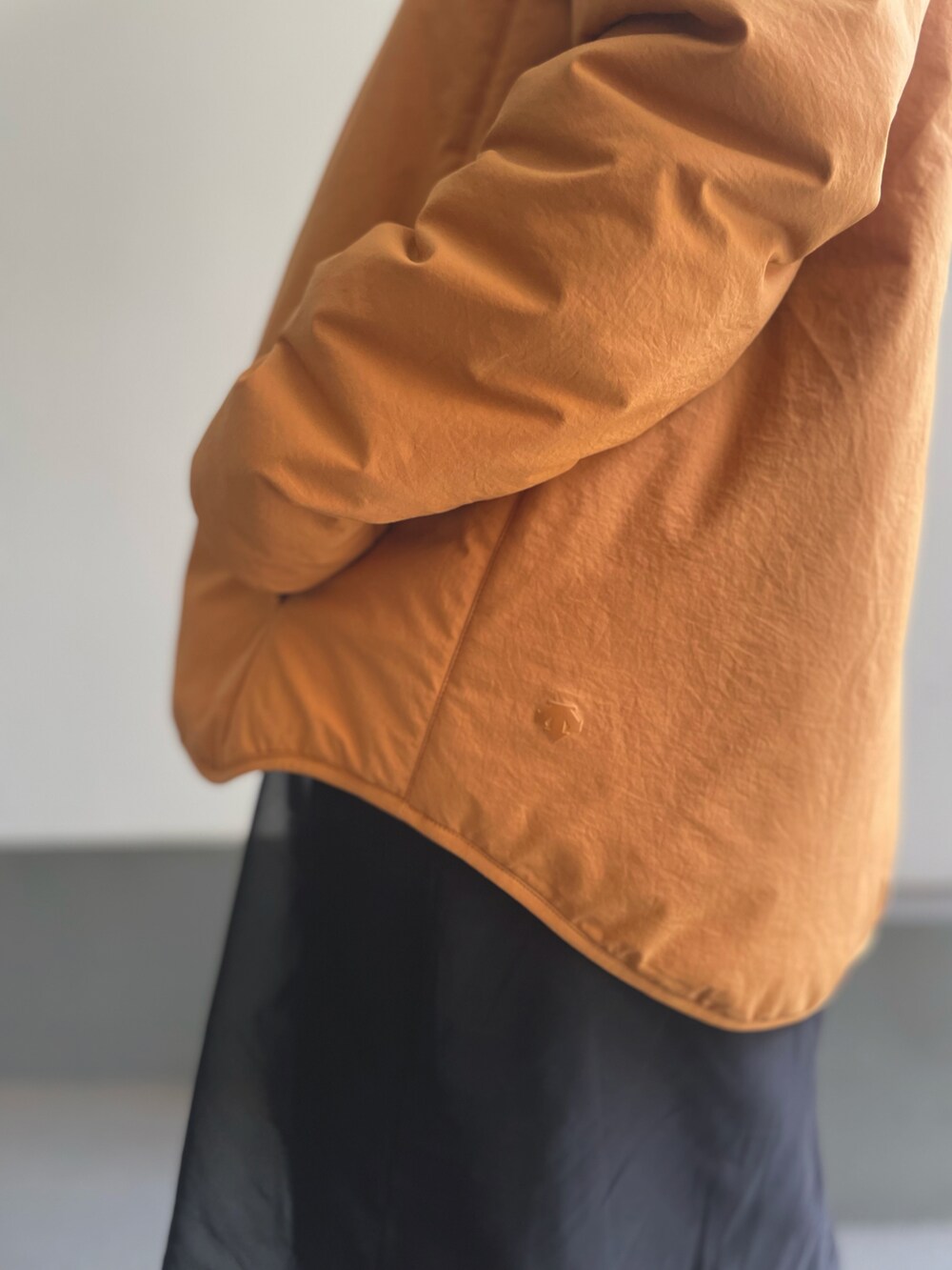 オレンジ系のノーカラーコート、ブラック系のワンピース、ベージュ系のブーツを着用したレディースの秋コーディネートの3枚目の写真