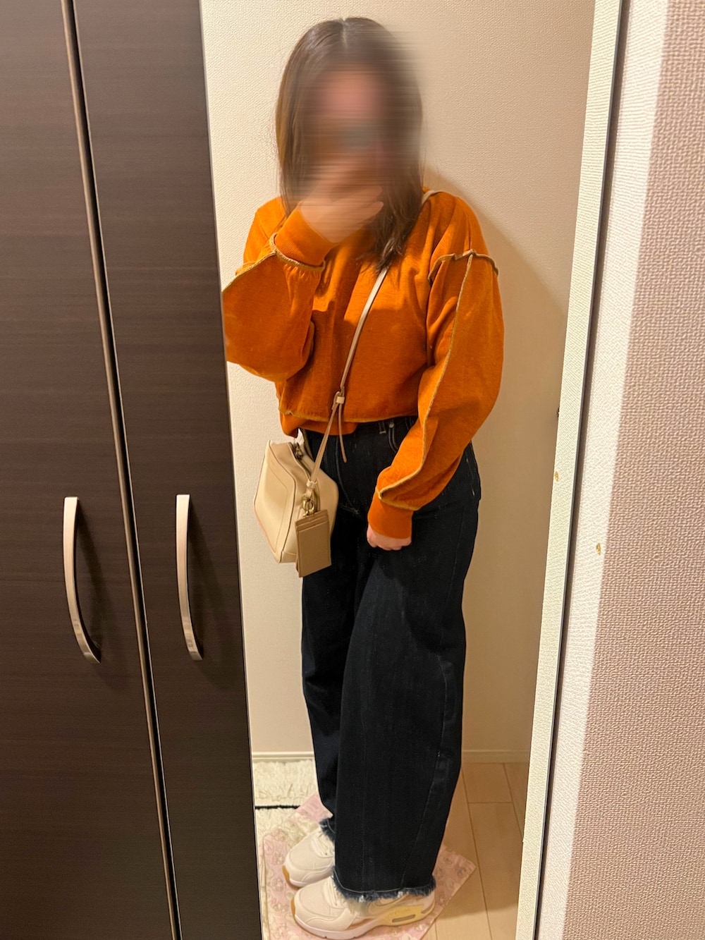 オレンジ系のパーカー、ベージュ系のショルダーバッグ、ブルー系のデニムパンツを着用したレディースの冬コーディネートの2枚目の写真