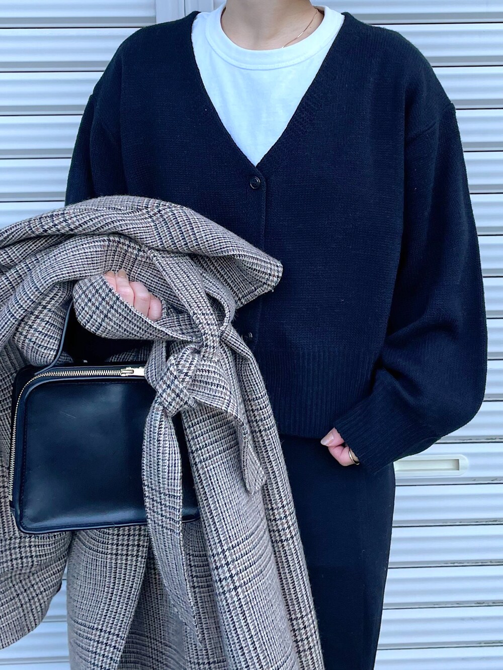 イエロー系のステンカラーコート、ブラック系のカーディガン/ボレロ、ブラック系のブーツを着用したレディースの冬コーディネートの2枚目の写真