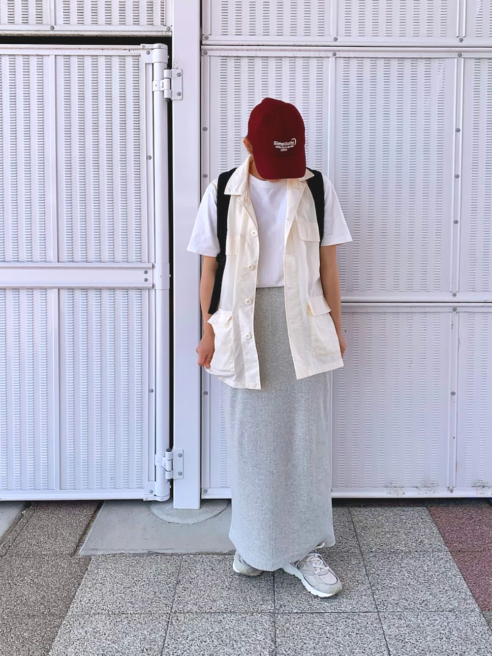 グレー系のスカート、ブラック系のバックパック/リュック、レッド系のキャップを着用したレディースの春コーディネートの2枚目の写真