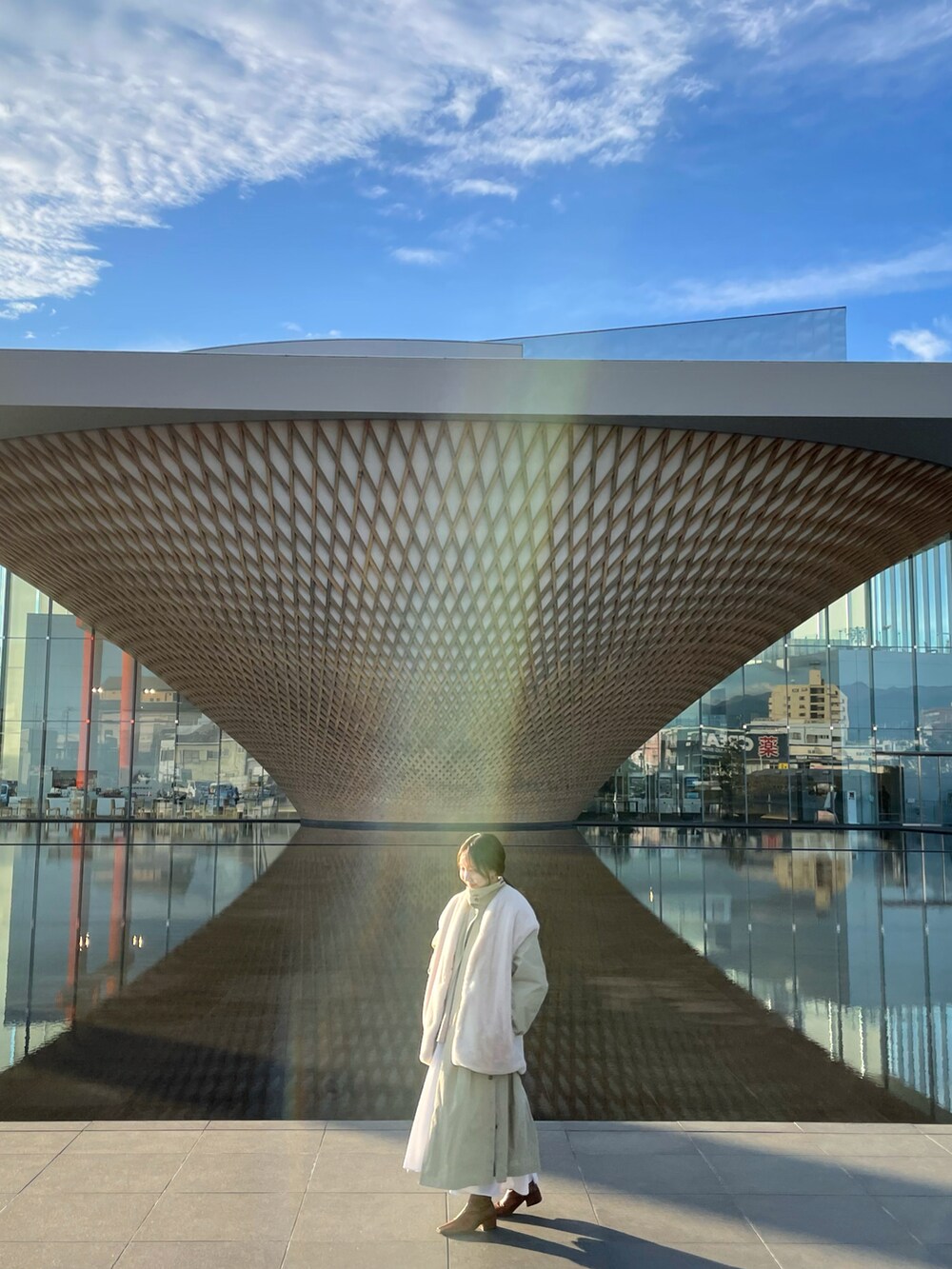 ホワイト系のベスト、グリーン系のステンカラーコート、ホワイト系のブーツを着用したレディースの冬コーディネートの2枚目の写真