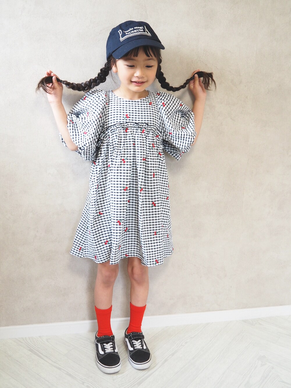 ブラック系のワンピース、レッド系のソックス/靴下、ブルー系のキャップを着用したキッズの春コーディネートの2枚目の写真