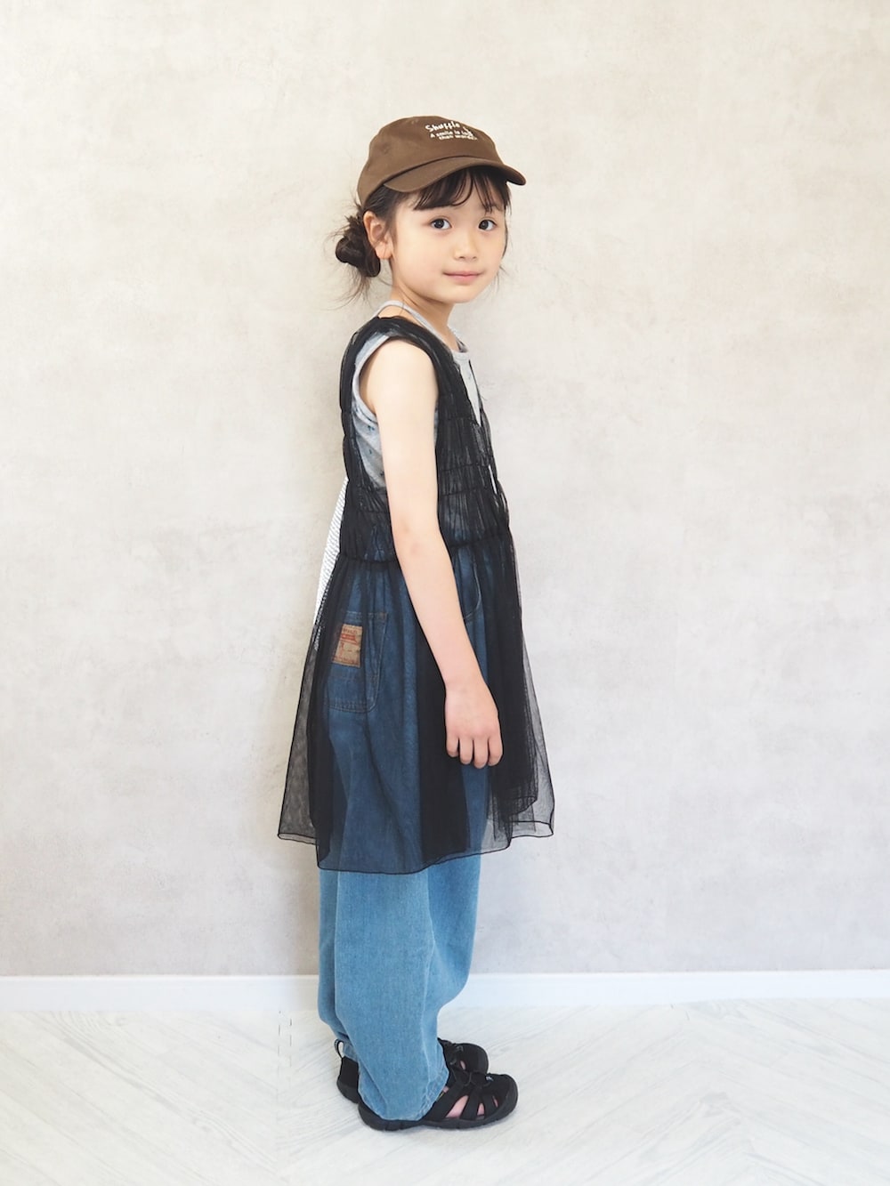 ブラック系のサンダル、ブラック系のワンピース、ブルー系のデニムパンツを着用したキッズの夏コーディネートの4枚目の写真